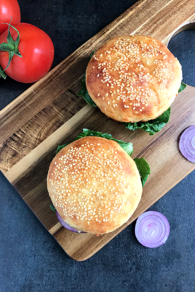 two Keto burger buns on a chopping board with a tomato and onion slices at the sides