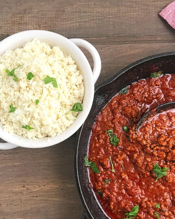 cauliflower rice in a white bowl with a skillet of tomato sauce